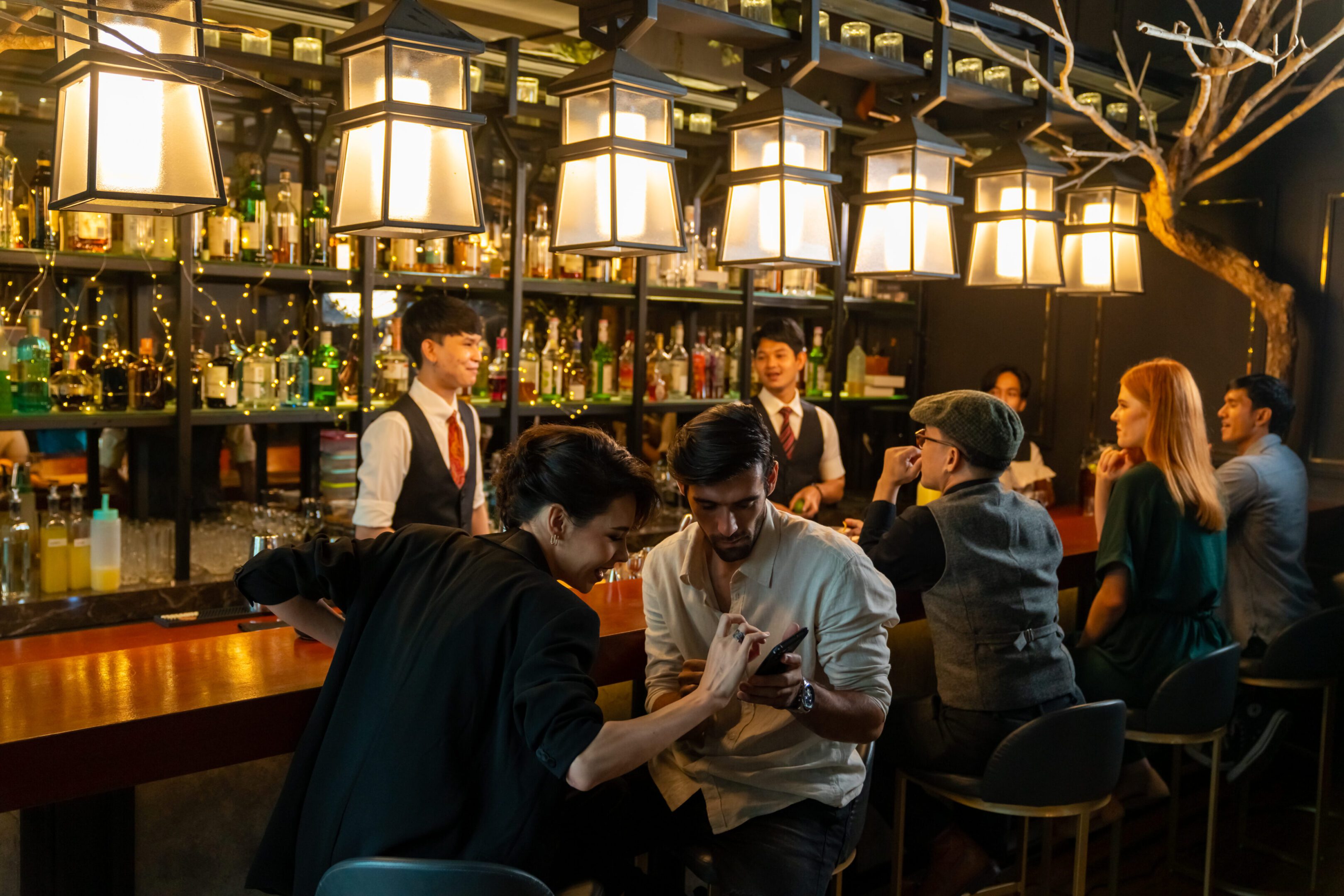 Caucasian man and woman using mobile phone together while hangout nightlife party at restaurant luxury bar. Attractive female romantic dating with boyfriend celebrating holiday event together at nightclub